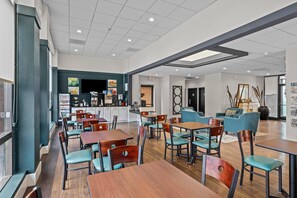 Un espacio interior amplio con varias mesas y sillas, una zona de cocina y un área de estar con sofás y sillones.