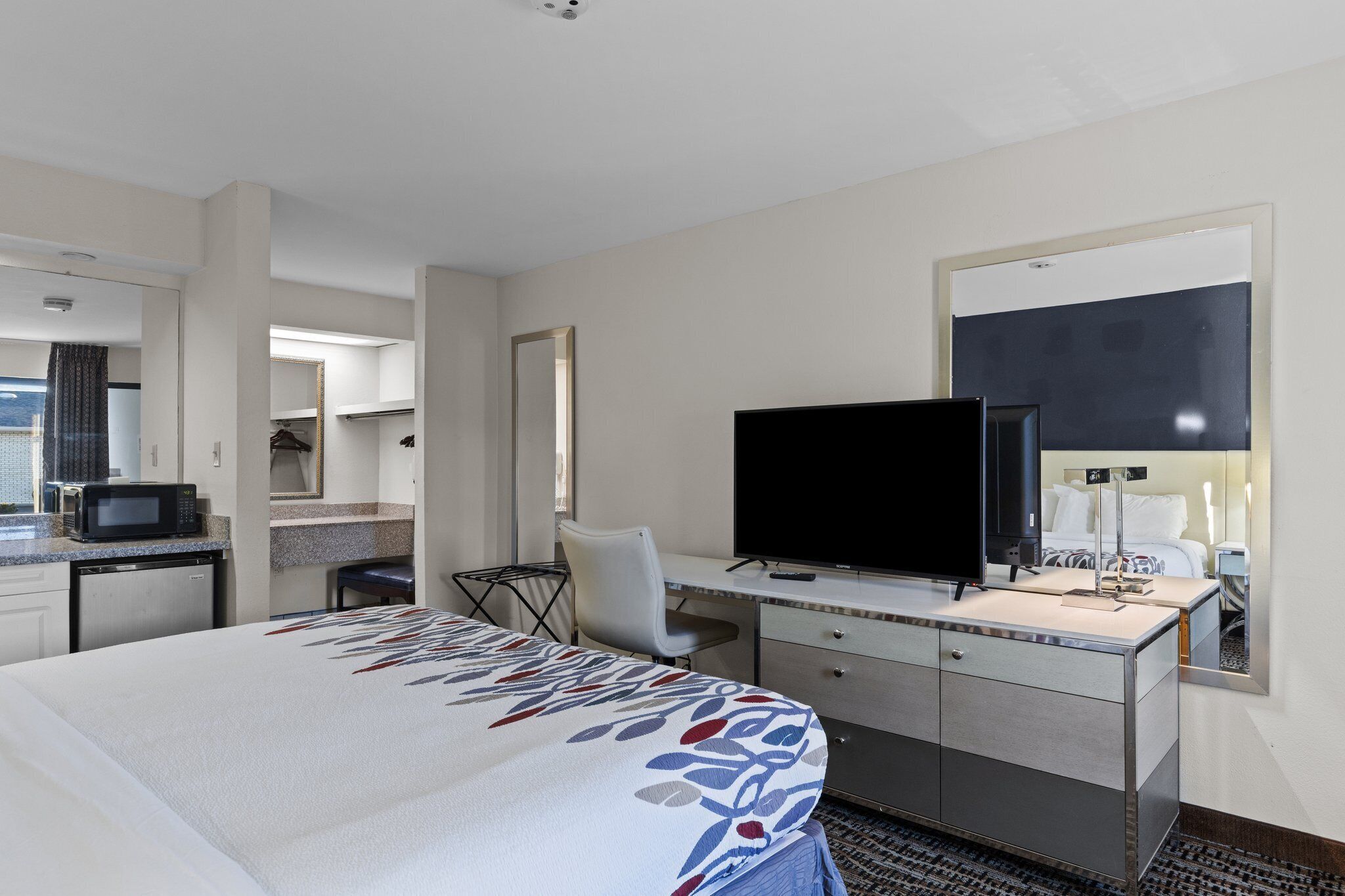 Une chambre d’hôtel comprenant un lit, un bureau avec un téléviseur à écran plat, un four à micro-ondes et une petite kitchenette.