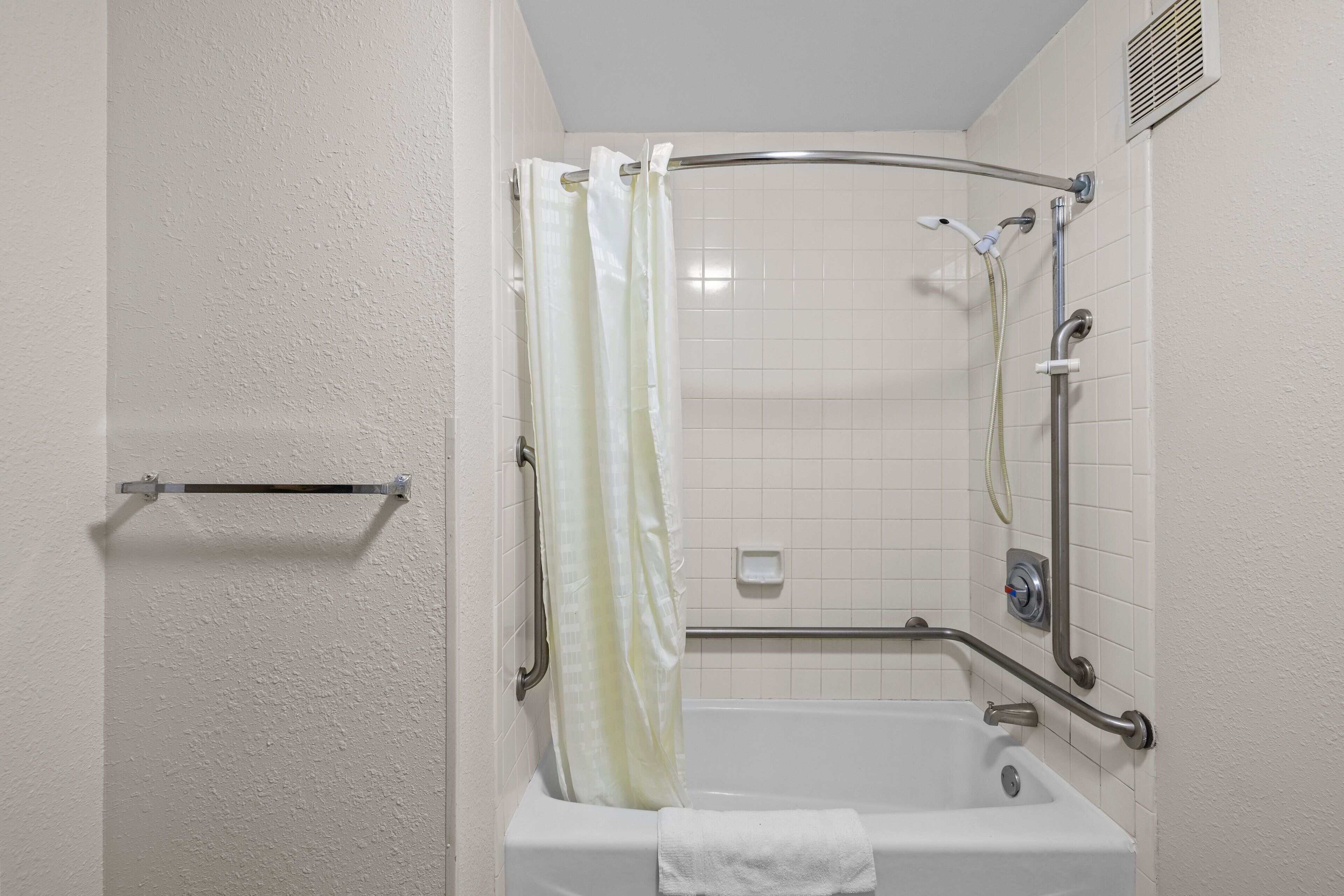 A corner shower with a grab bar, a white bathtub, and a towel hanging on the tub.