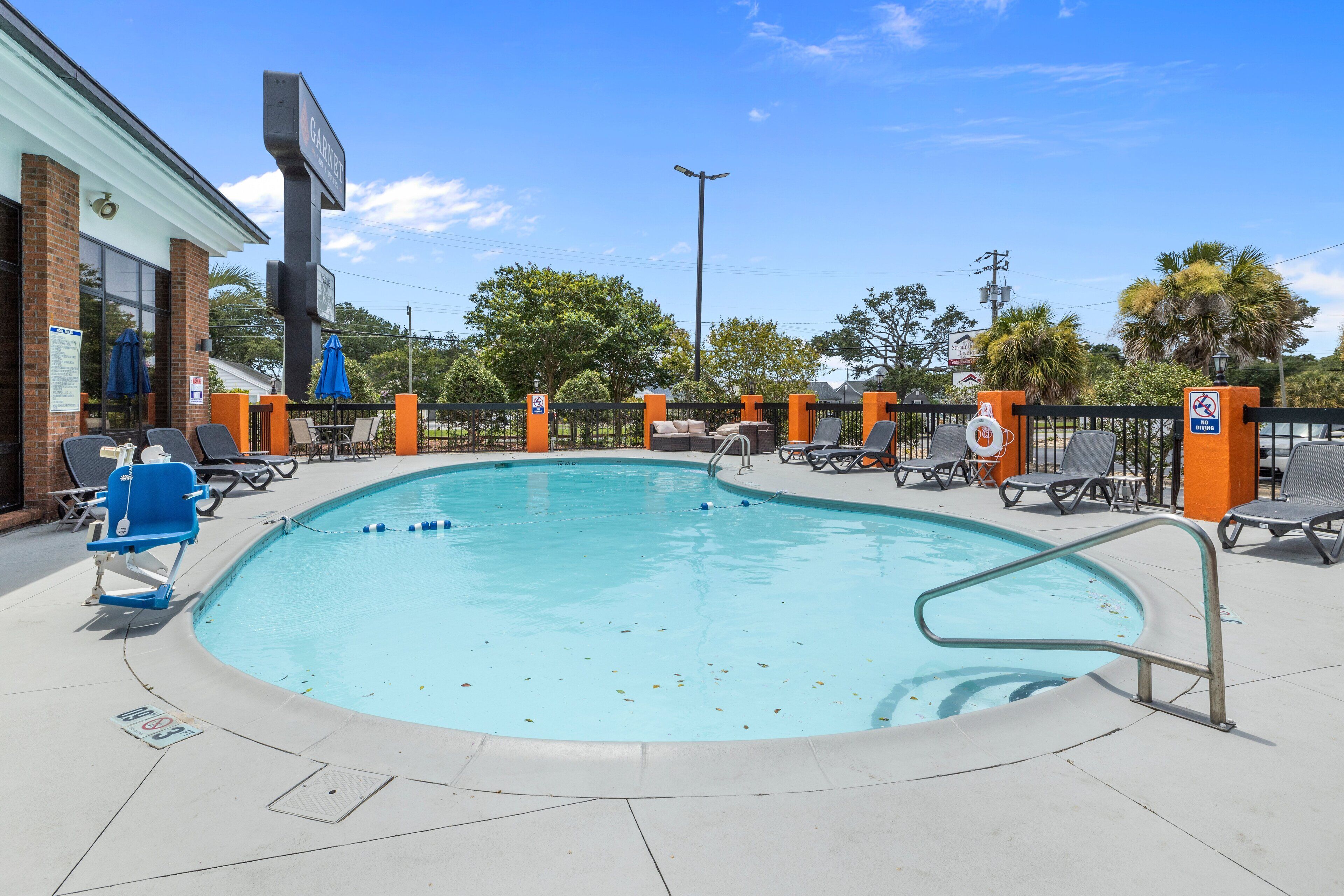A swimming pool with lounge chairs and umbrellas, surrounded by a fence and a building with a sign.