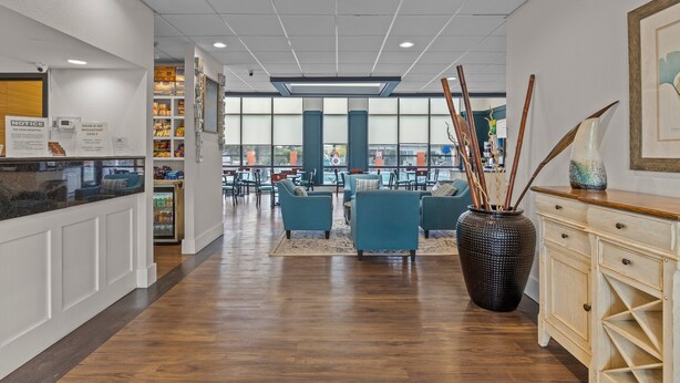 A spacious lobby with wooden flooring, seating areas, and a large vase with sticks. - Garnet Inn & Suites, Morehead City near Atlantic Beach (Morehead City)