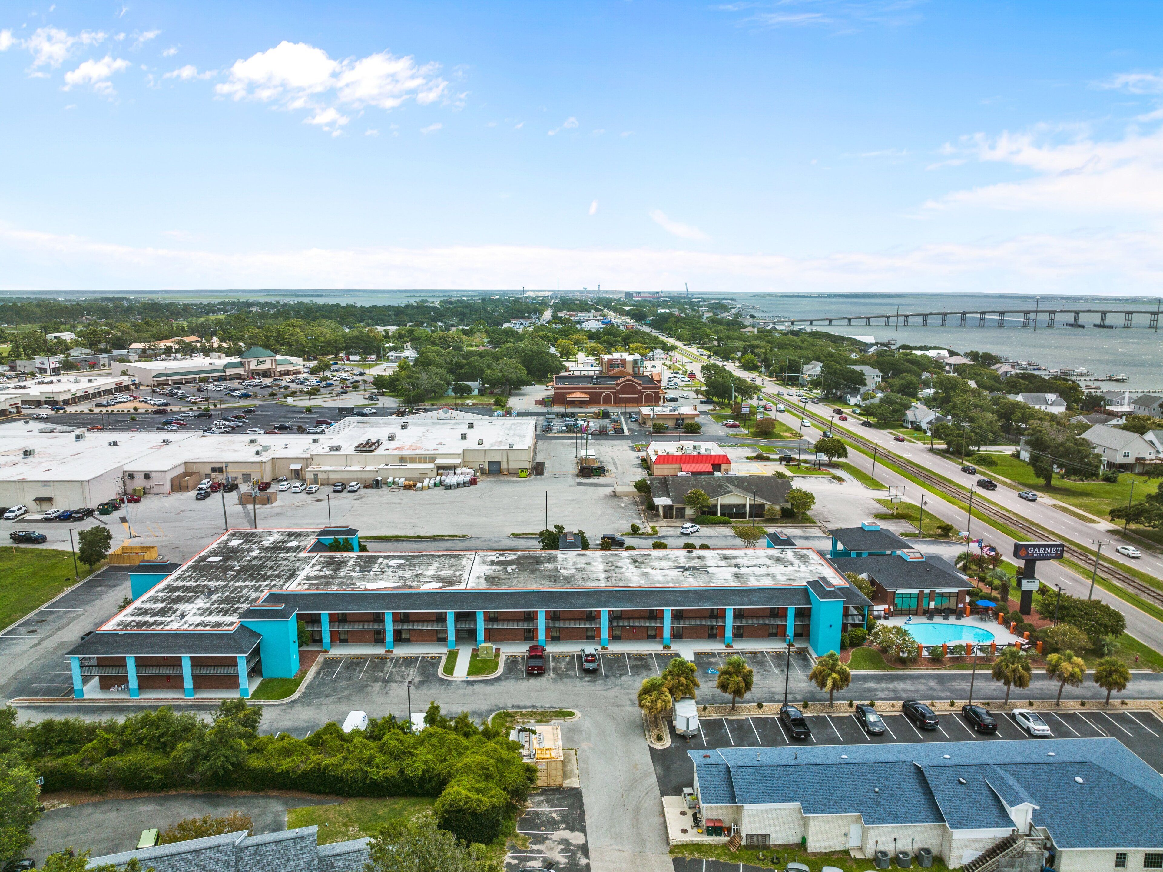 An aerial view of a commercial area with a parking lot, buildings, and a bridge in the background.