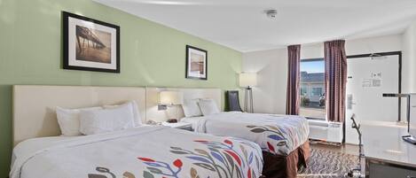 A hotel room with two beds, a desk, a chair, a window with curtains, and a picture on the wall.