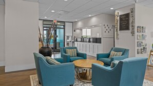 A modern lounge area with teal armchairs, a round wooden coffee table, and a kitchen in the background. - Garnet Inn & Suites, Morehead City near Atlantic Beach (Morehead City)