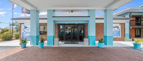 L’entrée d’un hôtel, avec une façade en briques, une décoration extérieure bleue et blanche, et des plantes en pot disposées à l’entrée.
