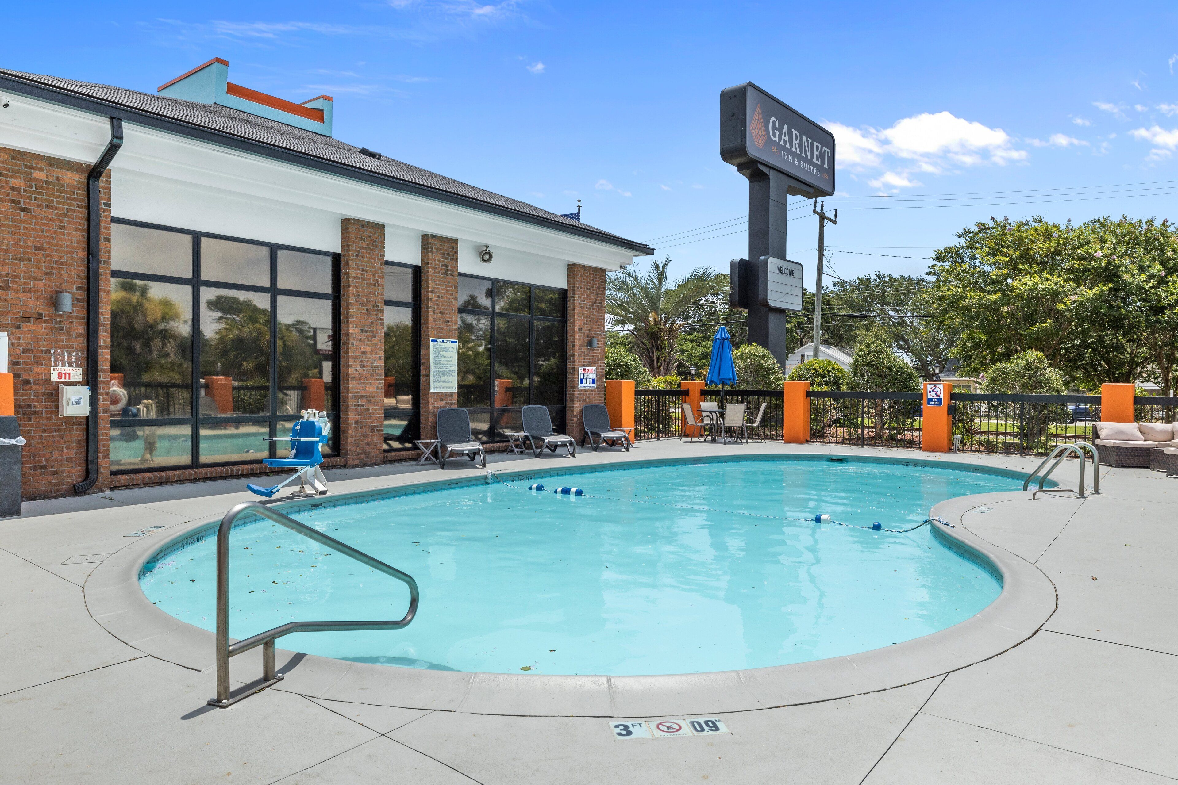 A pool area with lounge chairs, a brick building, and a sign for 'Garnet Inn & Suites'.