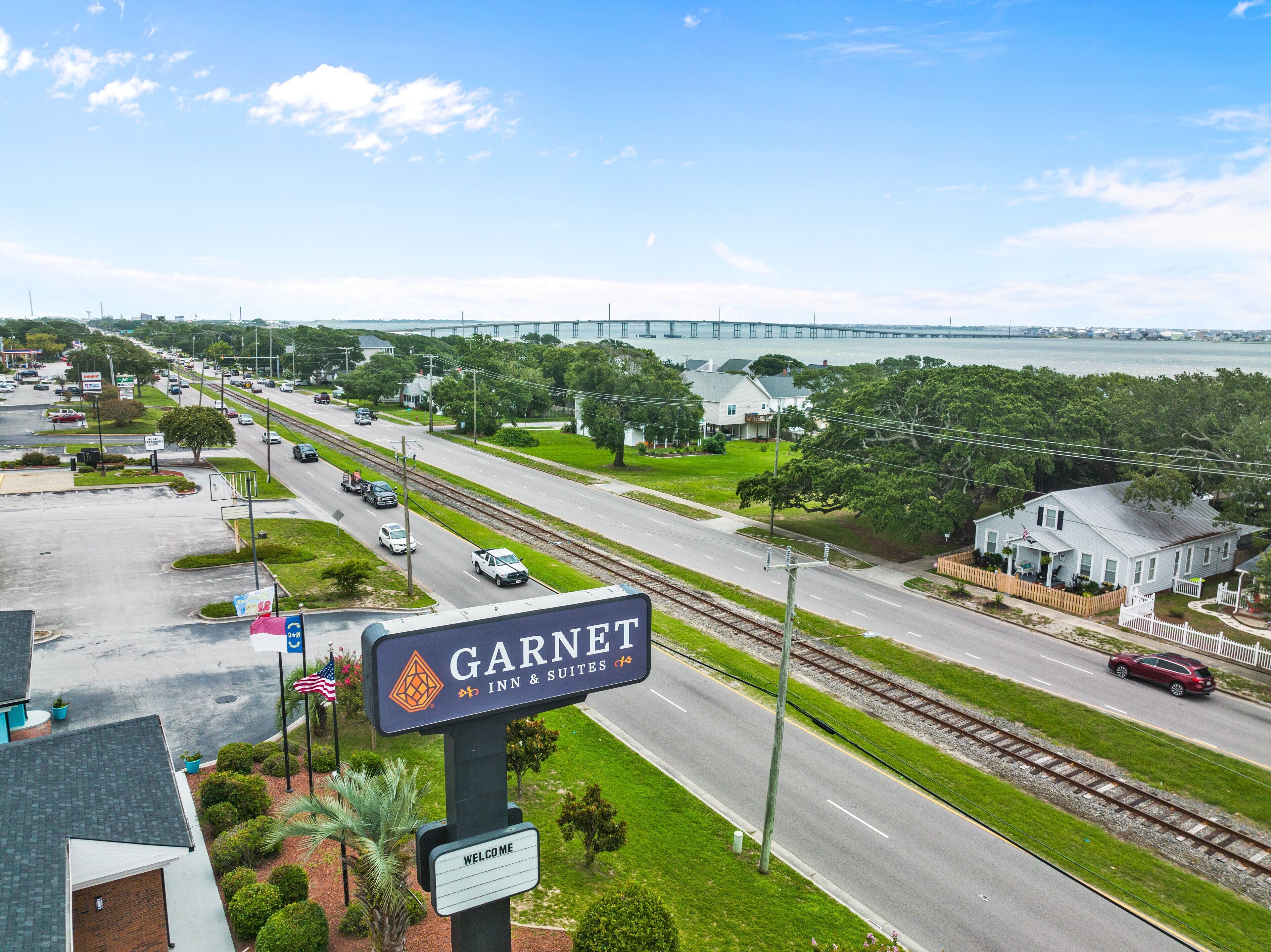 A street view with a sign for Garnet Inn & Suites, a road with cars, a bridge in the background, and greenery.