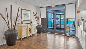 A reception area with a wooden floor, a light-colored cabinet, two large vases with branches, and a framed artwork on the wall. - Garnet Inn & Suites, Morehead City near Atlantic Beach (Morehead City)