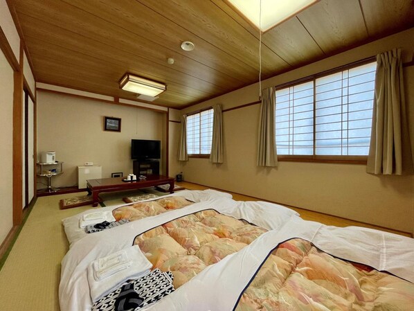A traditional Japanese-style room with tatami flooring, a low wooden bed, a television, and sliding doors. - Hitachi Hotel Crane (Hitachi)