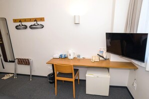 A hotel room with a wooden desk, a chair, a television, a small white refrigerator, a kettle, a telephone, and a coat rack with hangers. - Hitachi Hotel Crane (Hitachi)
