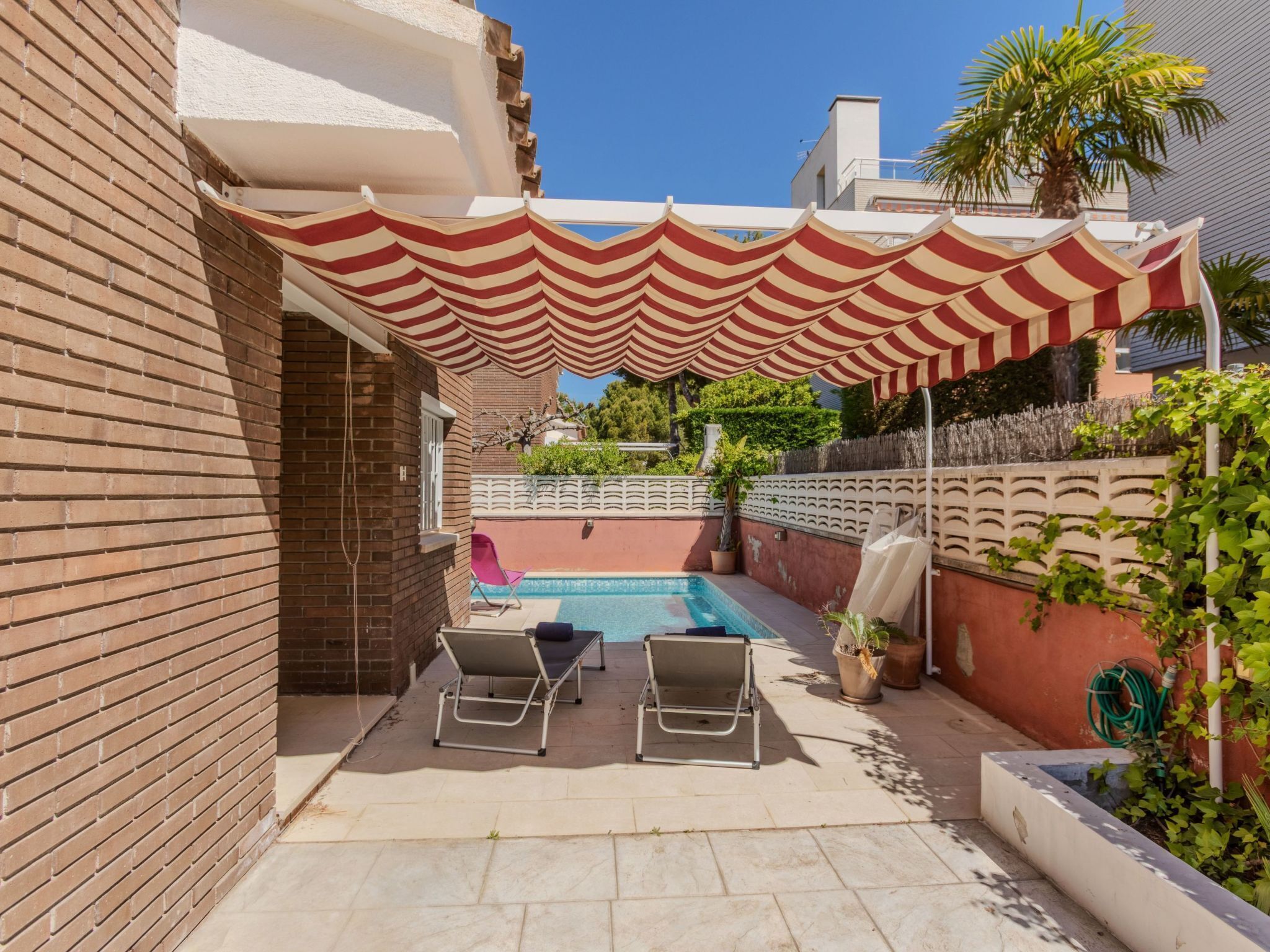 A rooftop pool area with striped awnings, two lounge chairs, and a view of the cityscape.
