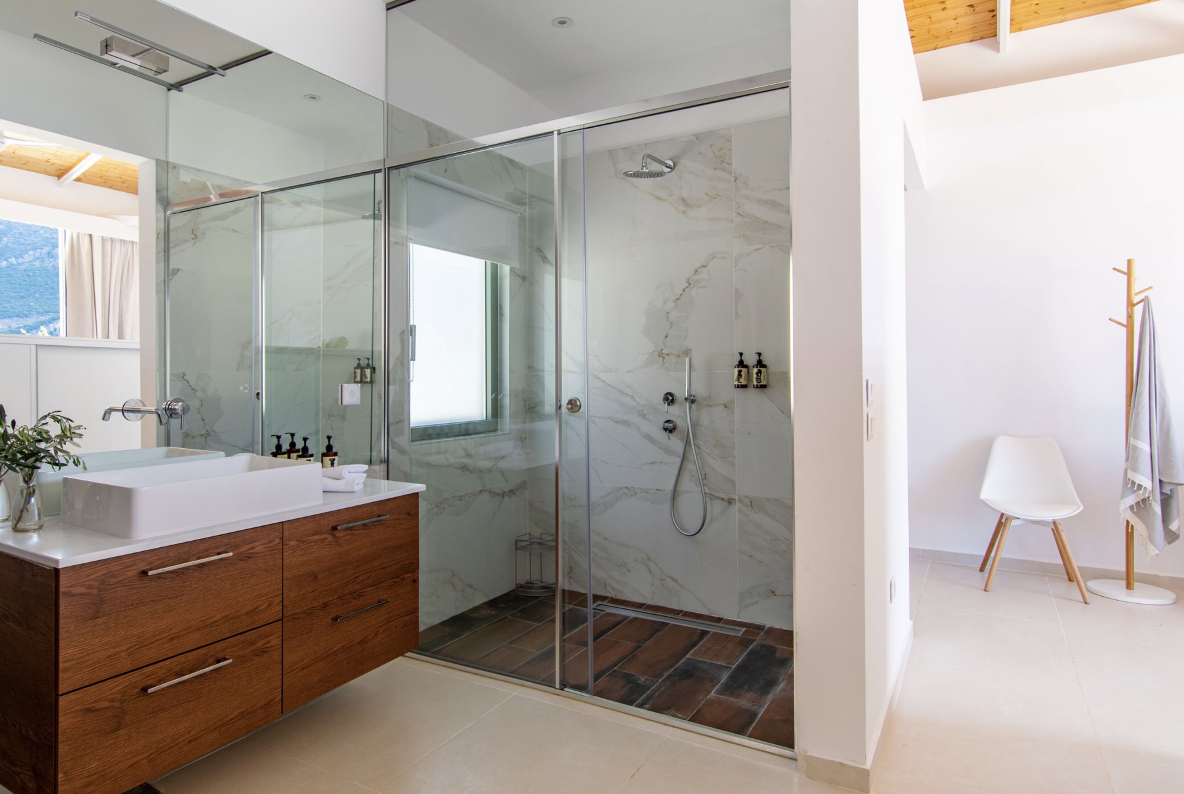 Een moderne badkamer met een glazen douchecabine, een houten wastafelmeubel en een grote spiegel.