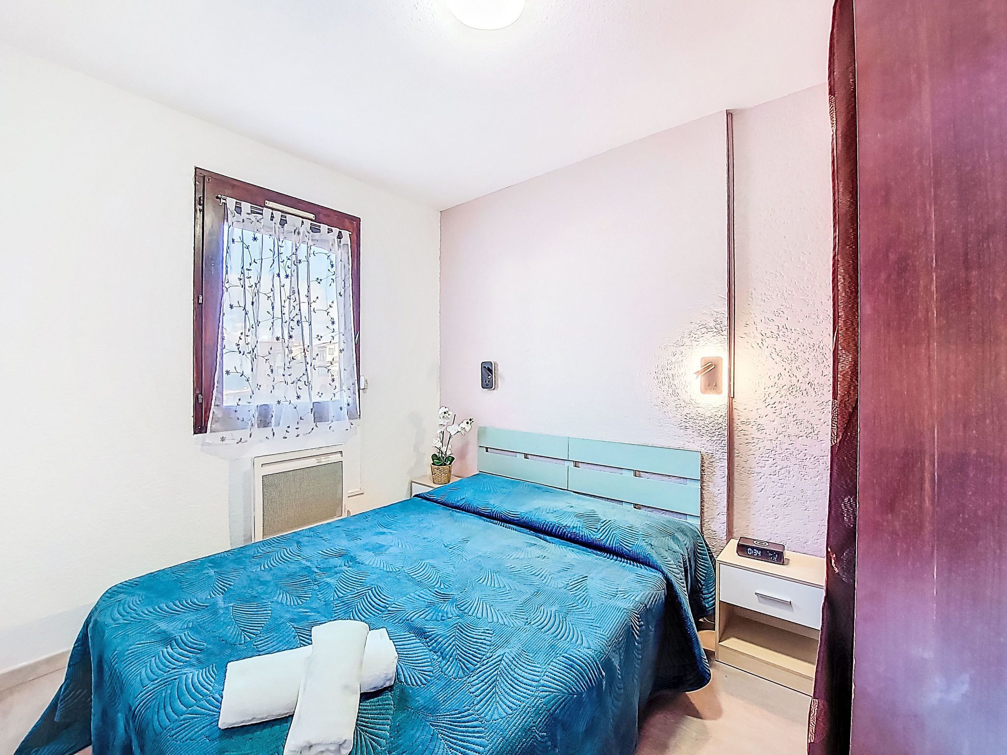 Un dormitorio con cama, una ventana con cortinas, una mesita de noche y un velador.
