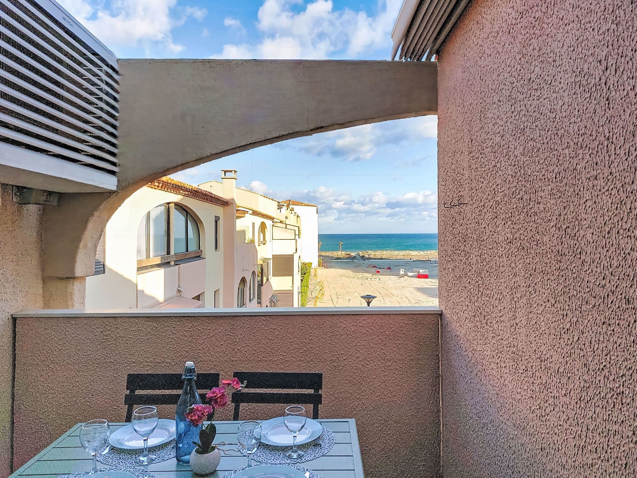 Ein Balkon mit Esstisch, der Blick auf einen Strand und ein Küstengebäude freigibt.