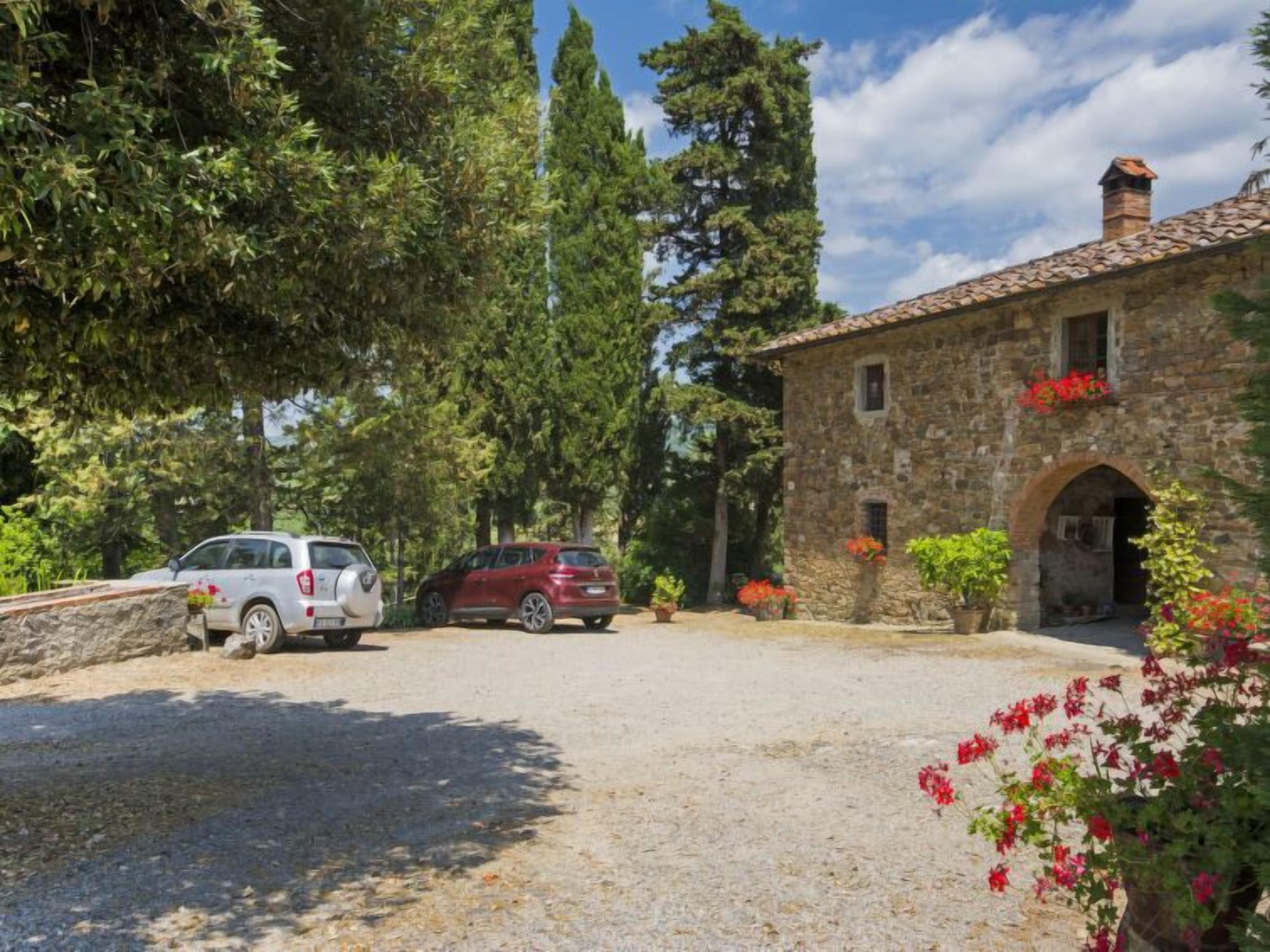 A stone building with an arched entrance, surrounded by trees and parked cars.