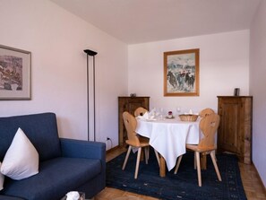 A dining area with a table set for two, a blue sofa, and wooden chairs.