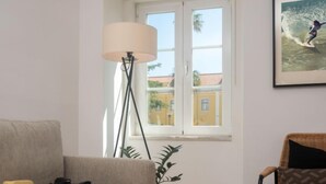 En stue med sofa, gulvlampe, stol, en potteplante og et billede i ramme på væggen.