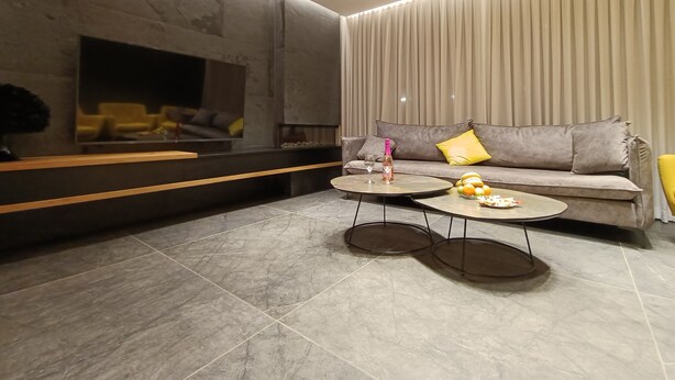 Un salón moderno con un sofá gris, dos mesas de centro redondas y un televisor de pantalla plana grande montado en una pared con textura.