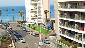 Un edificio de varios pisos con balcones, una rotonda con palmeras y vista al mar.