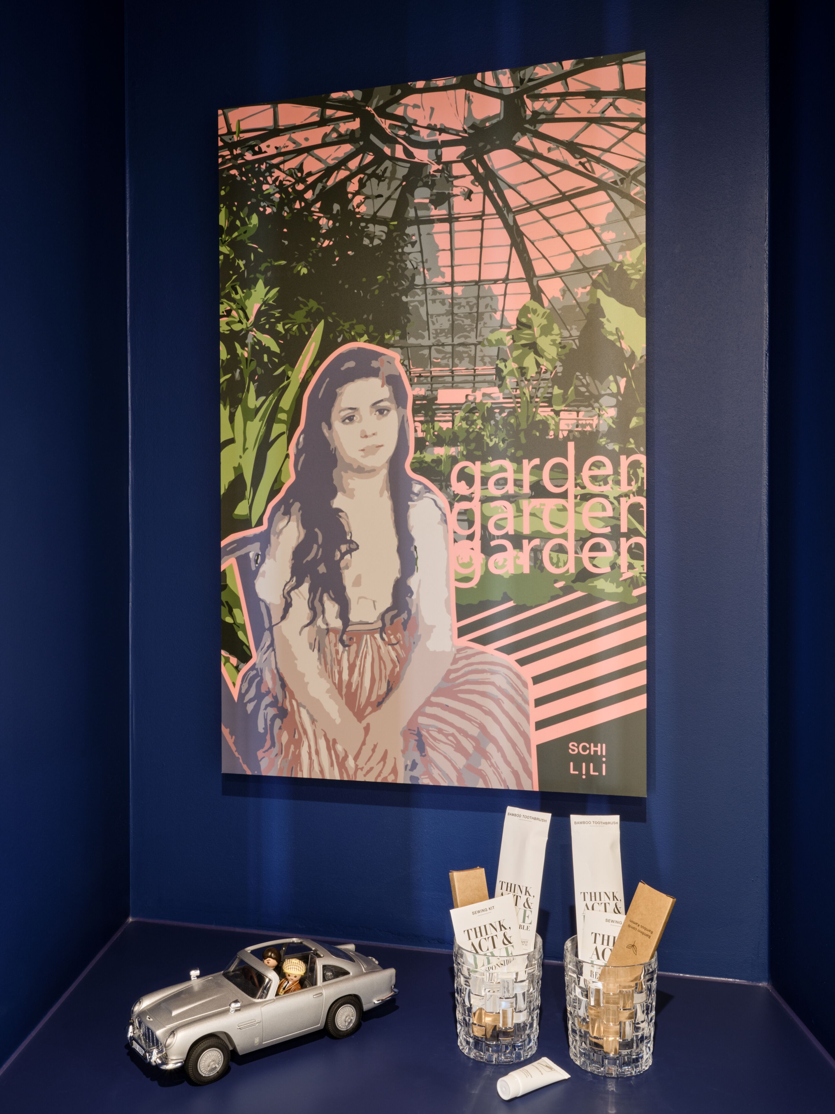 A framed artwork titled 'garden garden garden' by Schili Lili, a silver convertible toy car, and two glass bottles with 'Think Act & Ble' branded items.