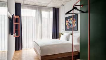 Ein modernes Hotelzimmer mit Holzboden, einem großen Bett mit weißer Bettwäsche, einem an der Wand befestigten Fernseher und einem Blumenbild.