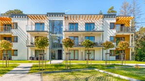 Un immeuble résidentiel moderne à plusieurs étages, doté de balcons, de grandes fenêtres et d’une pelouse bien entretenue.