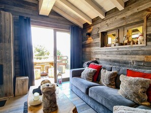 A cozy living room with a grey sofa, wooden walls, and a large window.