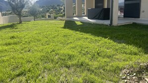 Et moderne hus med en velplejet græsplæne, en terrasse og bjergudsigt i baggrunden.