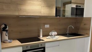 Et moderne køkken med træskabe, en sort komfur, en vask og en bordplade med elkedel og kaffemaskine.