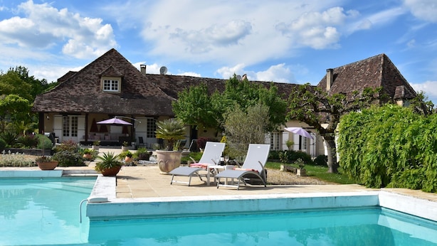 A poolside area with lounge chairs, a swimming pool, and a large house with a tiled roof. - Luxury Villa in Dordogne with Pool & Privacy (Port-Sainte-Foy-et-Ponchapt)