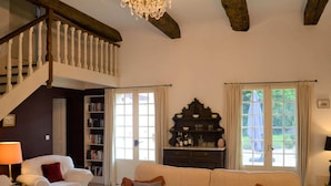 A living room with a white sofa, a red cushion, a bookshelf, a wooden cabinet, and a chandelier. - Luxury Villa in Dordogne with Pool & Privacy (Port-Sainte-Foy-et-Ponchapt)