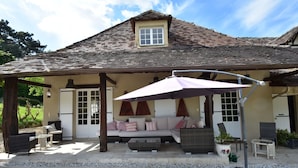 A covered patio area with a cushioned seating arrangement, a pergola with a canopy, and a small window. - Luxury Villa in Dordogne with Pool & Privacy (Port-Sainte-Foy-et-Ponchapt)