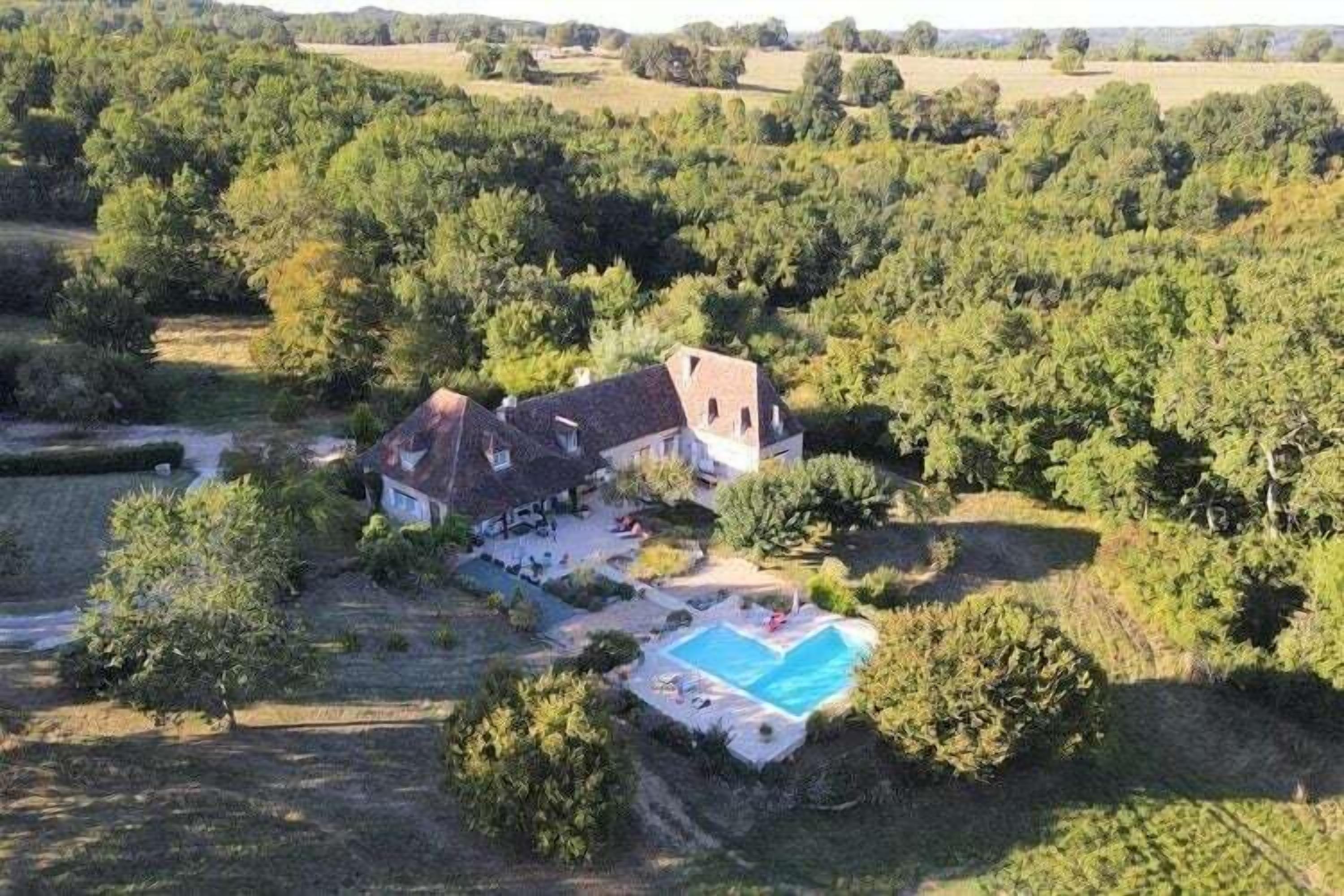 En vy från ovan av ett hus omgivet av tät vegetation, med en swimmingpool och en utomhusplats med sittmöbler.