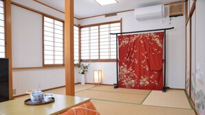 Et traditionelt japansk rum med tatamigulv, en skydedør med blomstermønstre, et lavt bord med tatami-måtte og et te-service samt en vægmonteret klimaanlæg.