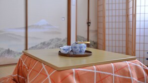 Et traditionelt japansk rum med tatamimåtter, et lavt træbord med en bakke med tepotte og kopper, og et maleri af et bjerg som baggrund.