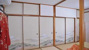 Et traditionelt japansk rum med tatamimåtter, shoji-skærme der viser et bjerglandskab, og en rød blomstergardin.