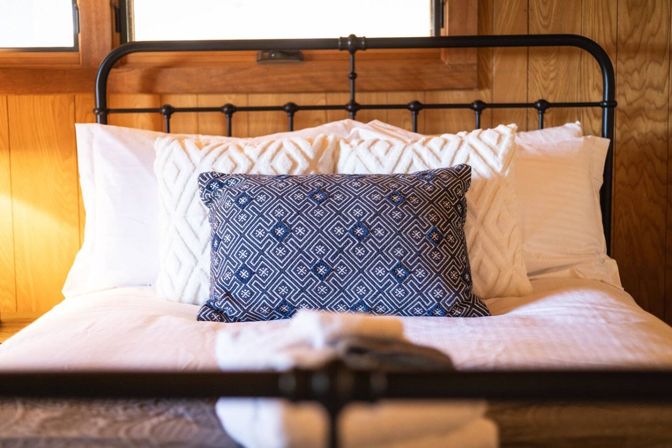 Un lit avec un cadre en métal, une literie blanche et des coussins à motifs.