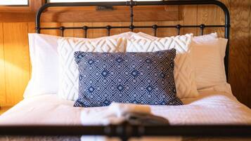Un lit avec un cadre en métal, une literie blanche et des coussins à motifs.