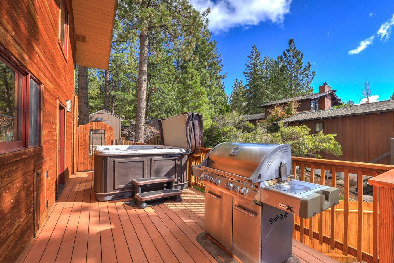 Una terraza de madera con jacuzzi, parrilla y zona de estar.