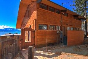 A wooden cabin with a large window, a wooden deck, and a view of mountains.