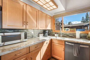 A kitchen with wooden cabinets, a microwave, a coffee maker, and a window with a view of a building and trees.