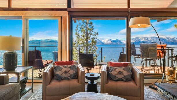 En rummelig balkon med udsigt over en sø og bjerge, møbleret med læderstole og et bord.