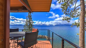 A wooden deck with outdoor furniture overlooking a lake with mountains in the background.
