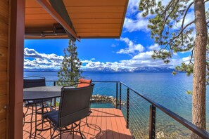 A wooden deck with outdoor furniture overlooking a lake with mountains in the background.
