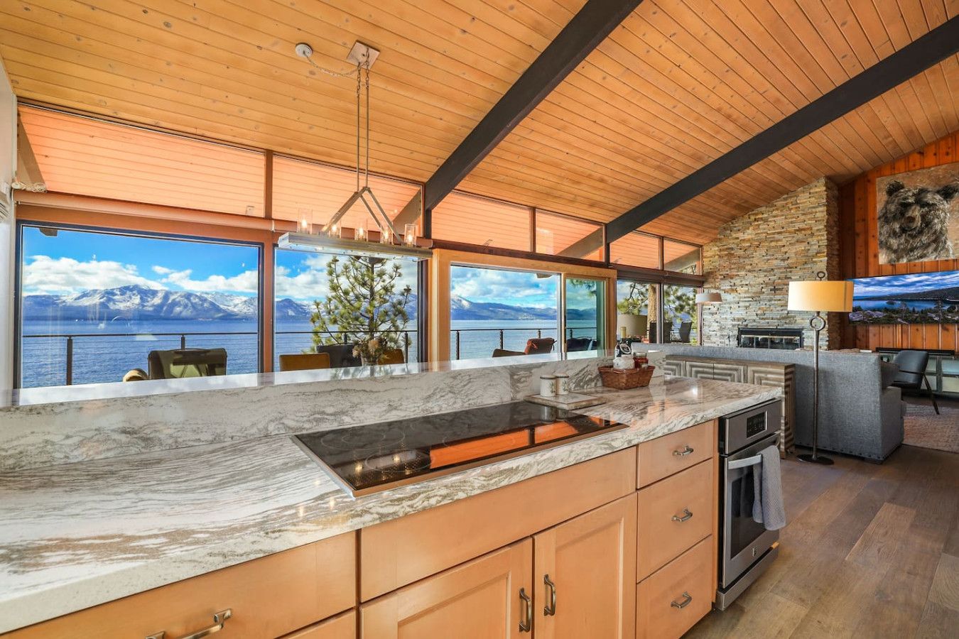 A modern kitchen with a large island, wooden cabinets, and a view of a lake and mountains.