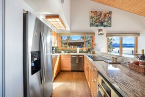 A modern kitchen with a stainless steel refrigerator, wooden cabinets, and a large island with a marble countertop.