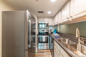 Enjoy cooking in this well-equipped kitchen with a refrigerator, microwave, and oven, as well as a double sink and granite countertop.
