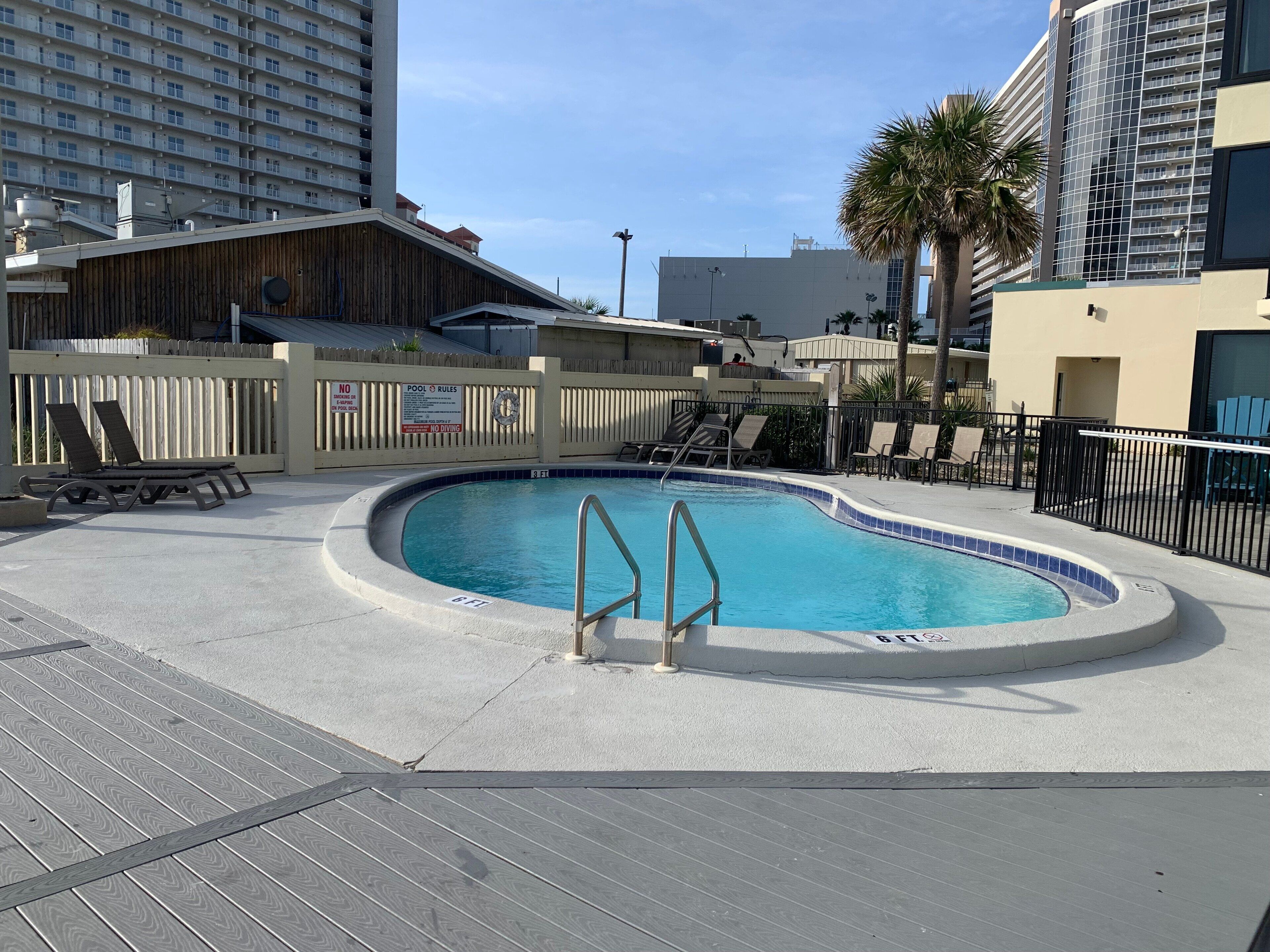 Une piscine avec une terrasse en bois, des chaises longues et une clôture.