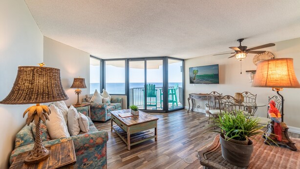 Een ruime woonkamer met een groot raam met uitzicht op de oceaan, een plafondventilator en een eethoek met terrasmeubels.
