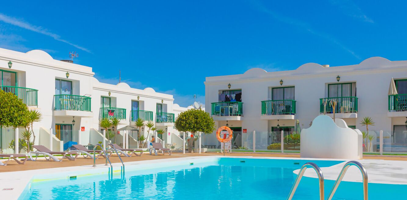 A pool area with white buildings, green balconies, and lounge chairs.